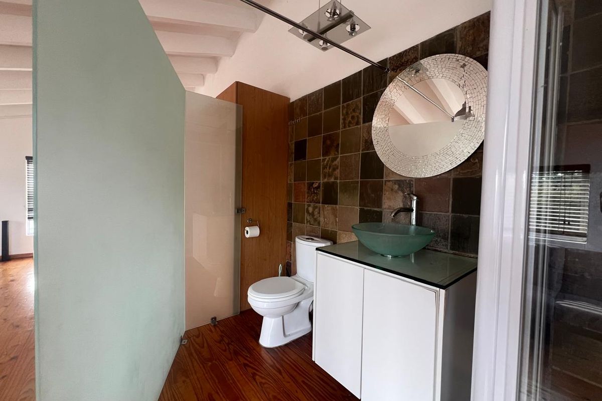 A modern bathroom featuring a vessel sink on a vanity cabinet, stone wall tiling, and timber flooring, with a glass shower partition.