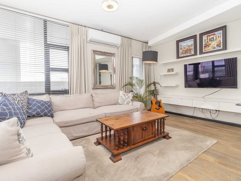 A well-maintained living room featuring laminate flooring, built-in media cabinetry, floating shelving, and a split-system air conditioning unit.