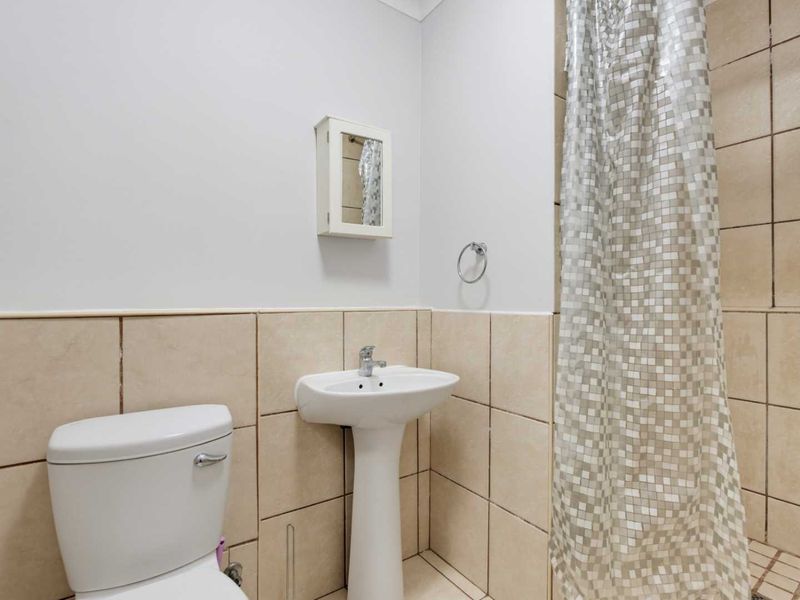 A functional bathroom featuring a pedestal basin, toilet, and shower area with neutral wall and floor tiling.
