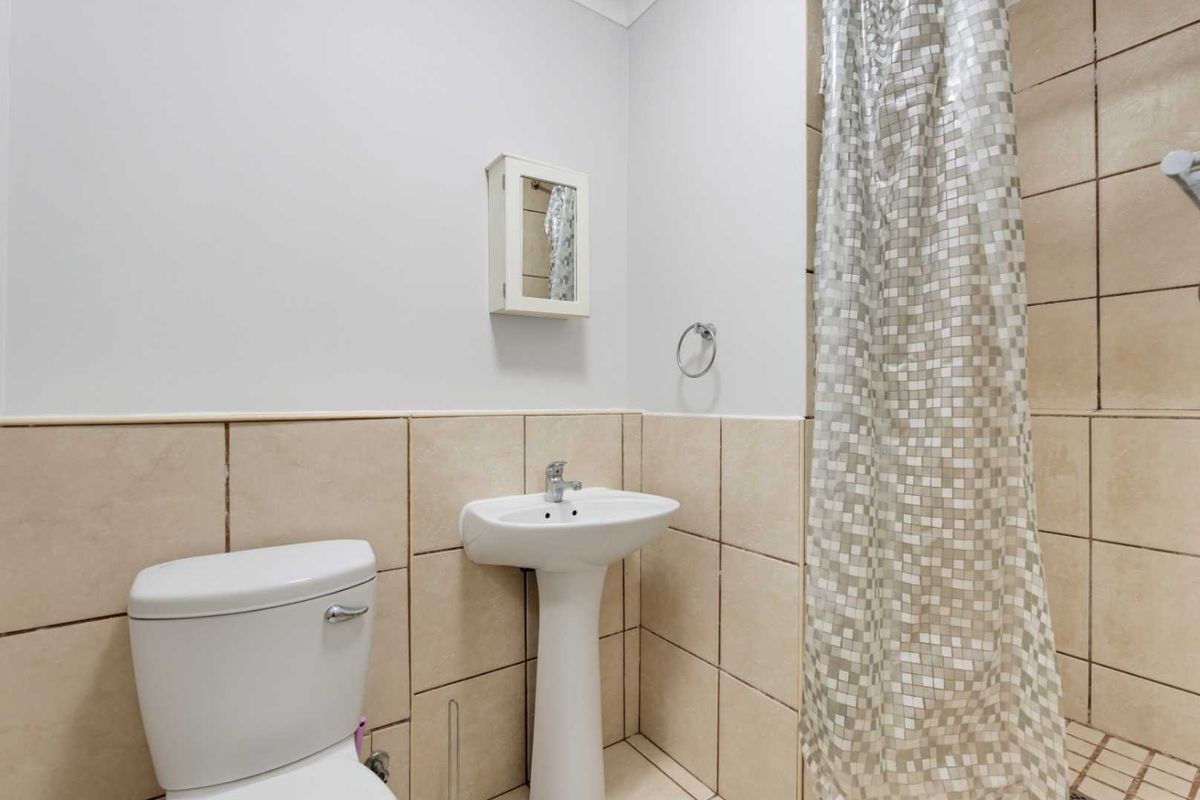 A functional bathroom featuring a pedestal basin, toilet, and shower area with neutral wall and floor tiling.