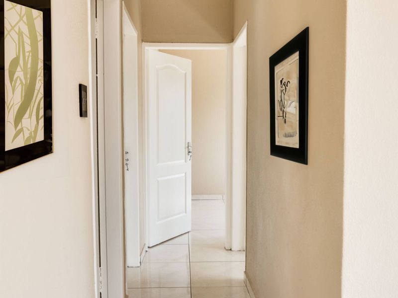A clean, neutral-toned hallway featuring tiled flooring and multiple internal doorways leading to adjacent rooms.