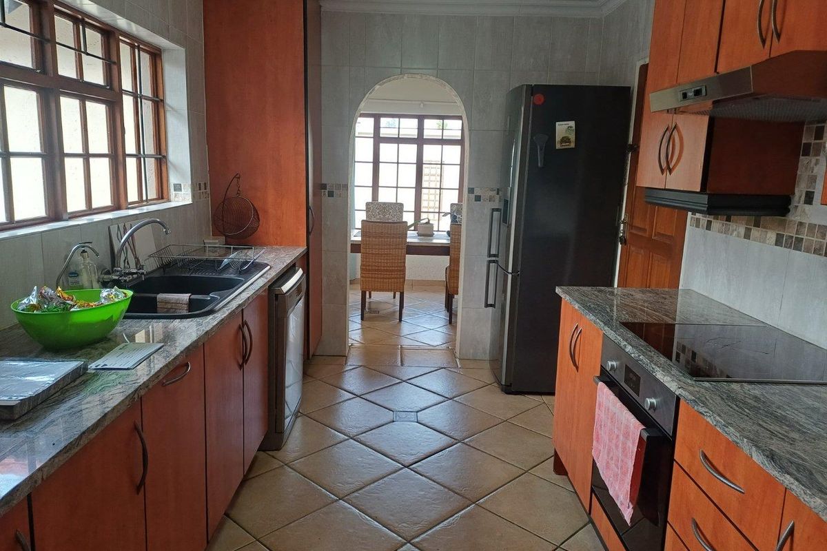 A functional kitchen featuring wooden cabinetry, granite countertops, tiled flooring, and integrated appliances, with an arched doorway leading to an adjacent dining area.