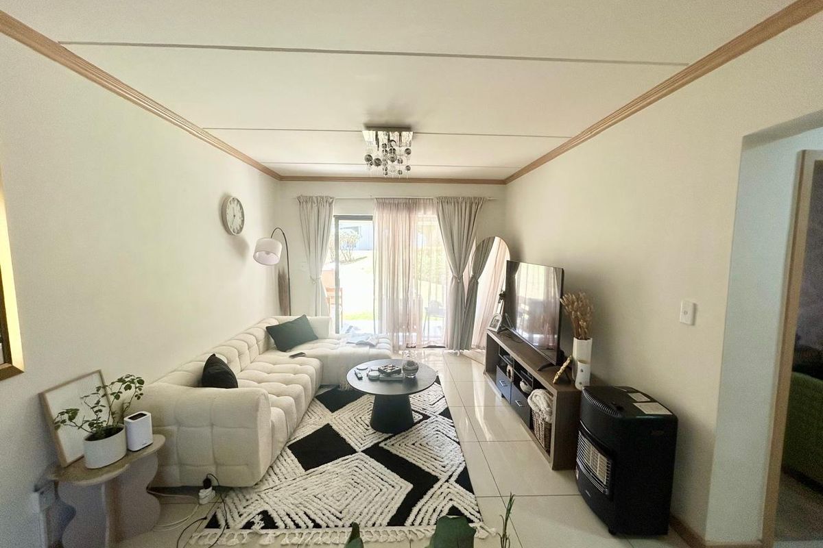 A well-maintained living room featuring tiled flooring, ceiling molding, and a sliding glass door that provides natural light and access to the outdoors.