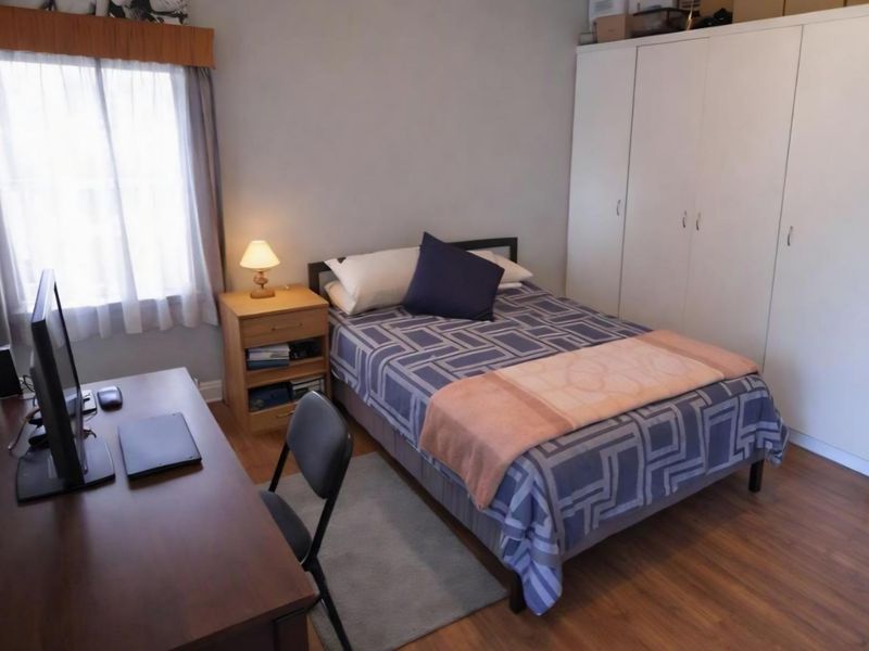 A functional bedroom featuring laminate flooring, a built-in wardrobe, and a window providing natural light.