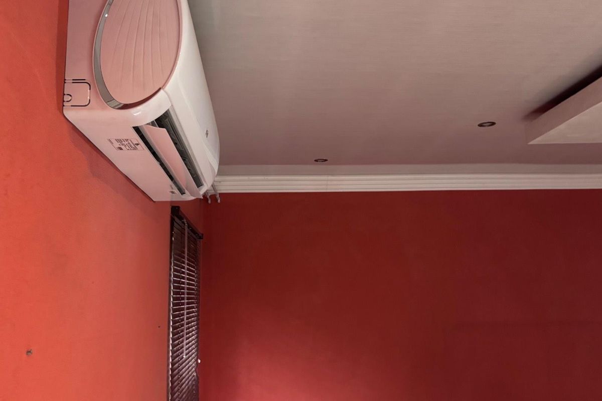 A corner view of a room featuring a wall-mounted air conditioning unit, recessed ceiling lighting, and venetian blinds.