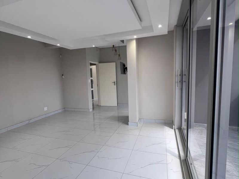 A bright, modern living area featuring polished porcelain floor tiles, a contemporary recessed ceiling with downlights, and large sliding glass doors.