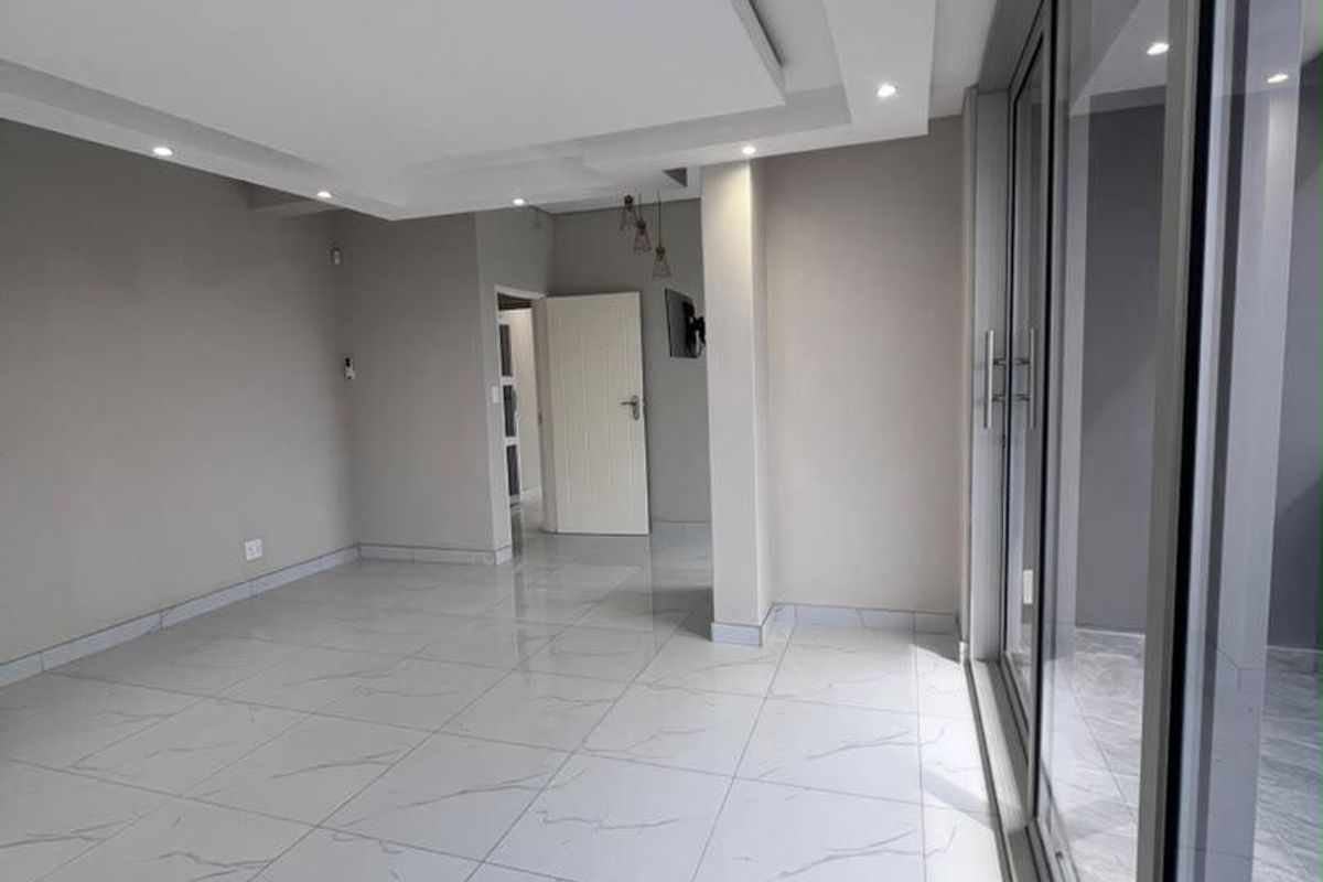 A bright, modern living area featuring polished porcelain floor tiles, a contemporary recessed ceiling with downlights, and large sliding glass doors.