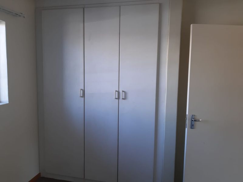 A clean, empty bedroom featuring a functional built-in wardrobe with simple cabinetry and a standard internal door.