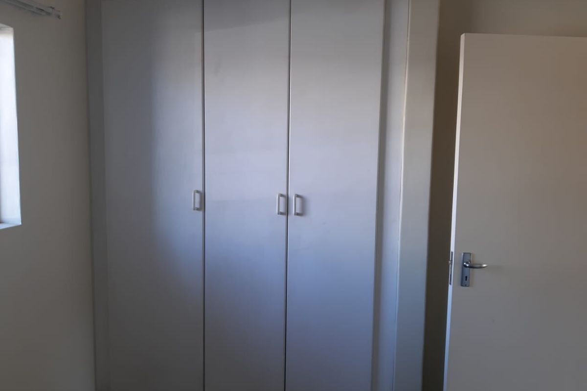 A clean, empty bedroom featuring a functional built-in wardrobe with simple cabinetry and a standard internal door.