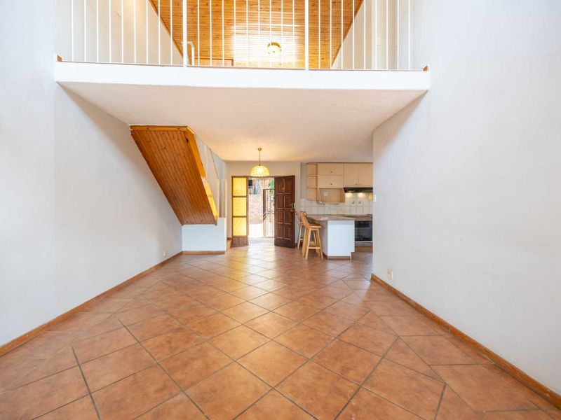 Spacious open-plan living area featuring a mezzanine level, tiled flooring, and a functional kitchen with built-in cabinetry and appliances.