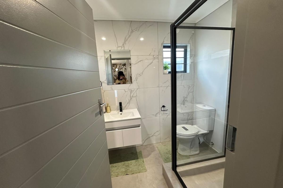Modern bathroom featuring marble-look wall tiles, a sleek vanity with black fixtures, and a glass-enclosed shower.