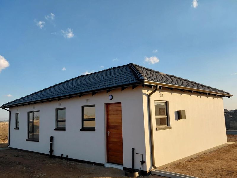 A view of the rear exterior of a modern house featuring a tiled roof, timber door, and aluminium window frames.