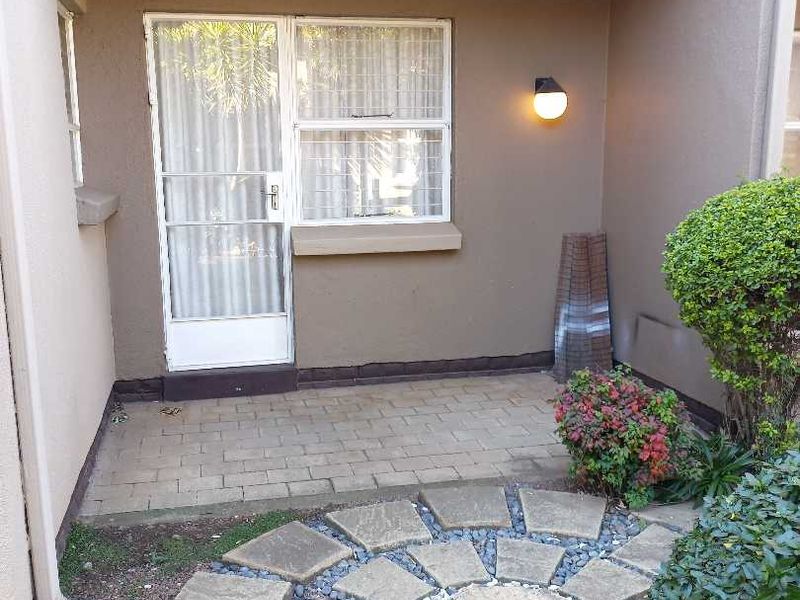 A covered patio area featuring paved flooring, a security gate, and a decorative stone garden path leading to the entrance.
