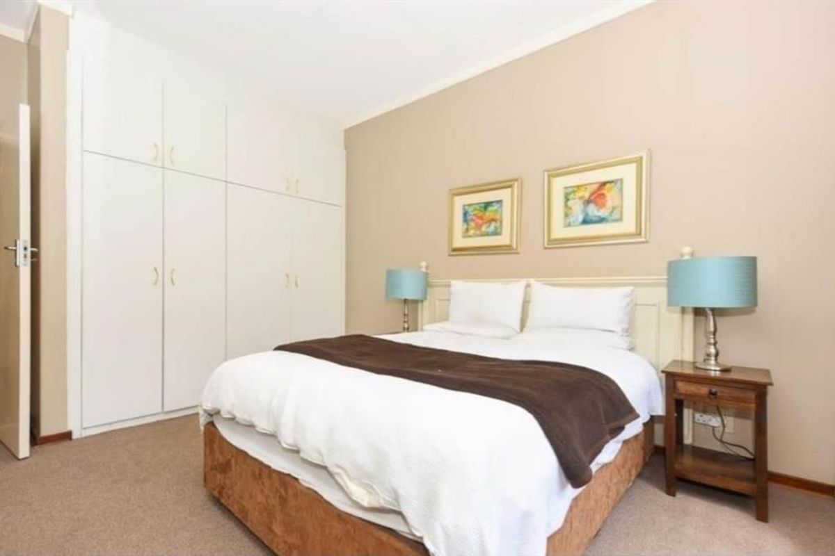 A well-maintained bedroom featuring neutral wall tones, carpeted flooring, and ample built-in cupboard storage space.