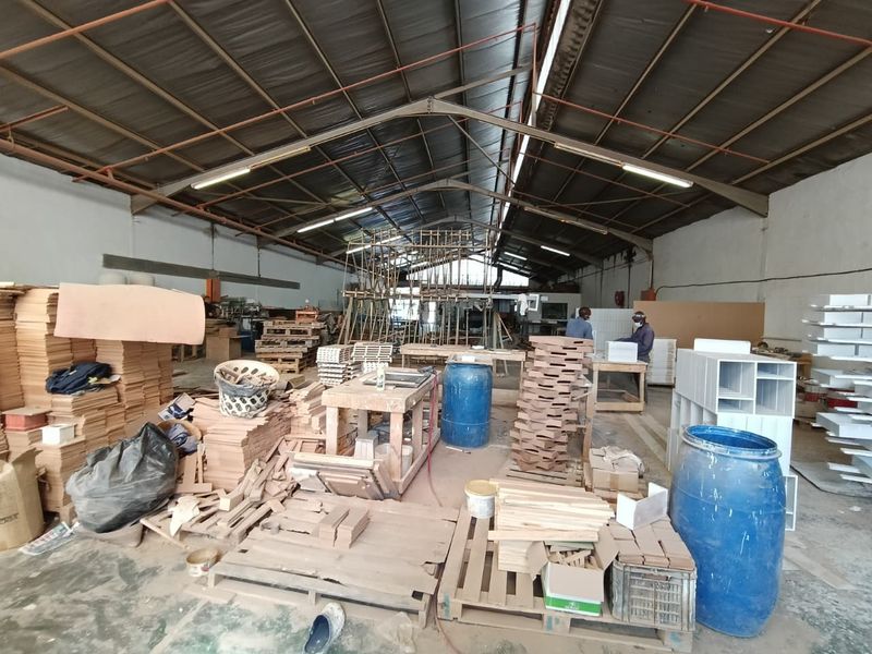 Spacious industrial workshop area featuring high ceilings with exposed steel trusses, fluorescent lighting, and durable concrete flooring, suitable for manufacturing or storage operations.