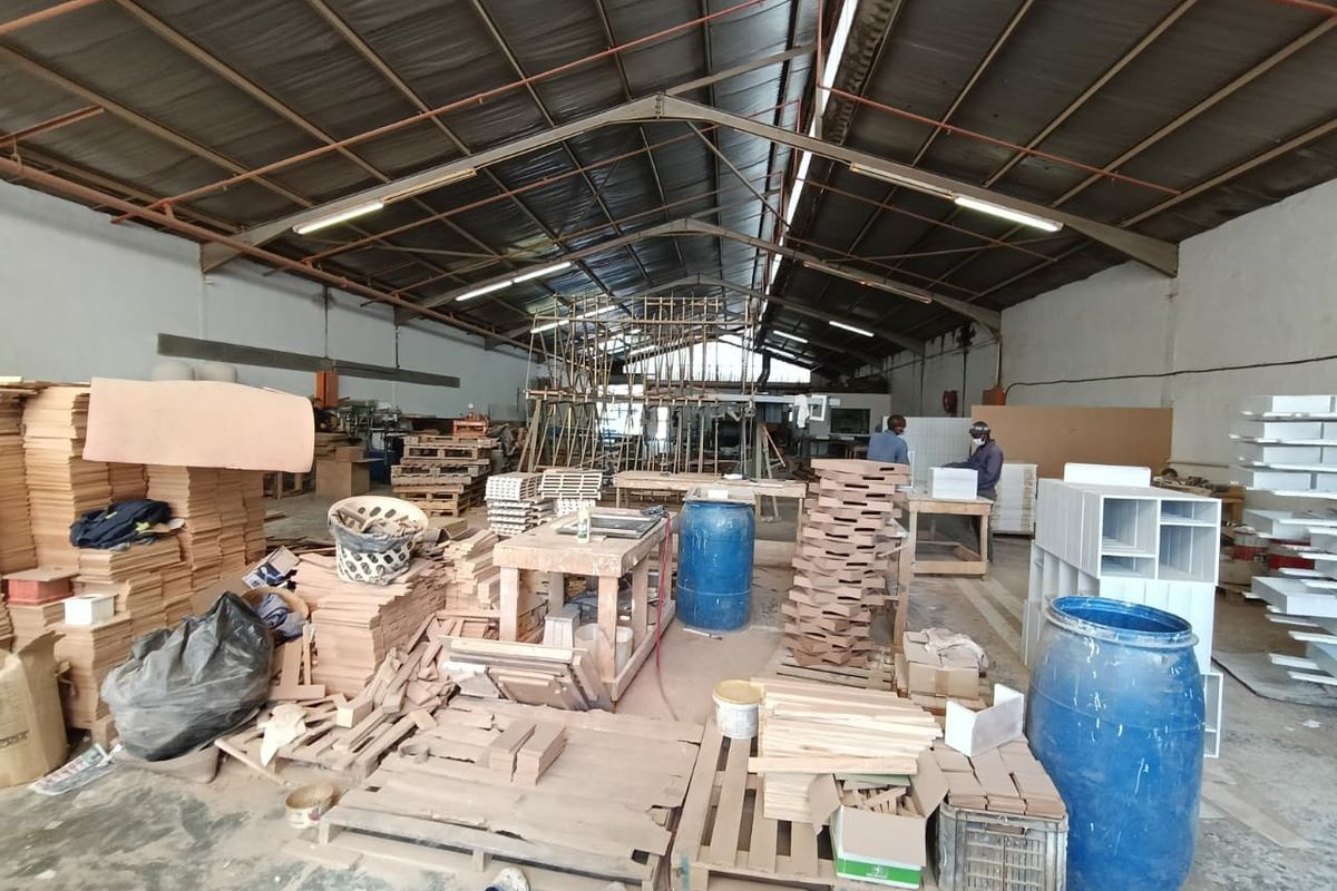 Spacious industrial workshop area featuring high ceilings with exposed steel trusses, fluorescent lighting, and durable concrete flooring, suitable for manufacturing or storage operations.