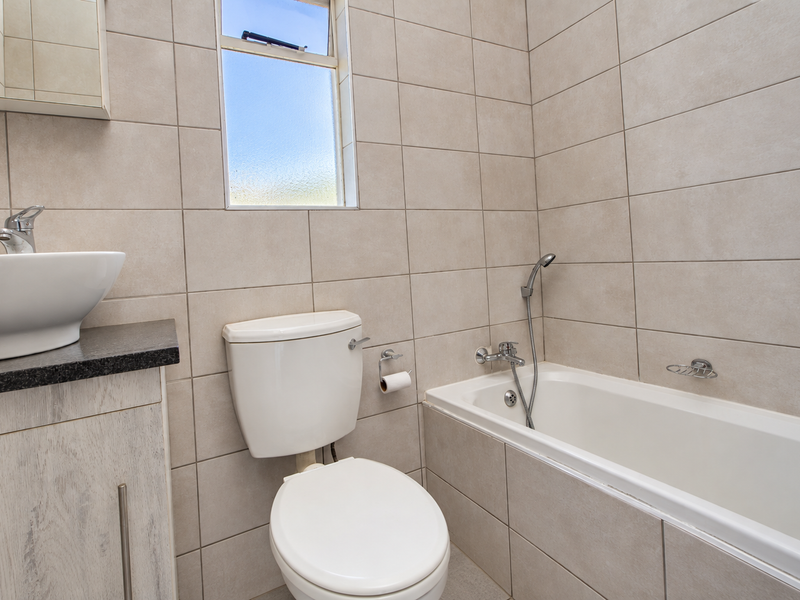 A modern bathroom featuring a vessel sink on a granite vanity, a toilet, and a tiled bathtub with a handheld shower mixer.