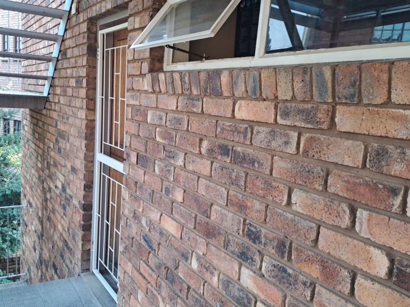 Exterior view of an apartment building featuring face brick walls, a security gate, and an external metal staircase.