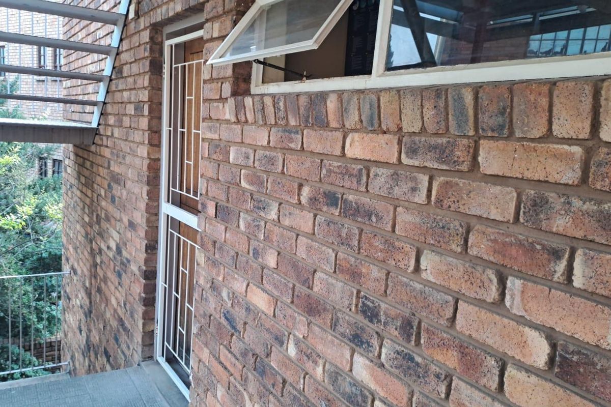 Exterior view of an apartment building featuring face brick walls, a security gate, and an external metal staircase.