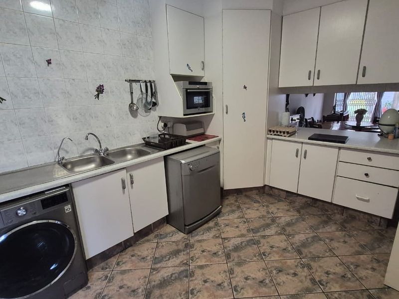 Functional kitchen featuring white cabinetry, laminate countertops, tiled backsplash, and integrated microwave, with tiled flooring throughout.