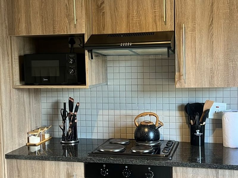 A well-maintained kitchen featuring wood-grain laminate cabinetry, granite countertops, a tiled backsplash, and integrated appliances including an oven, hob, and extractor fan.