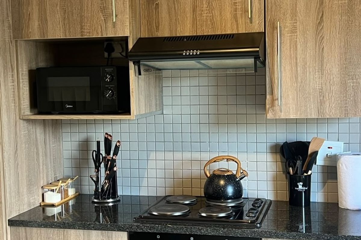 A well-maintained kitchen featuring wood-grain laminate cabinetry, granite countertops, a tiled backsplash, and integrated appliances including an oven, hob, and extractor fan.
