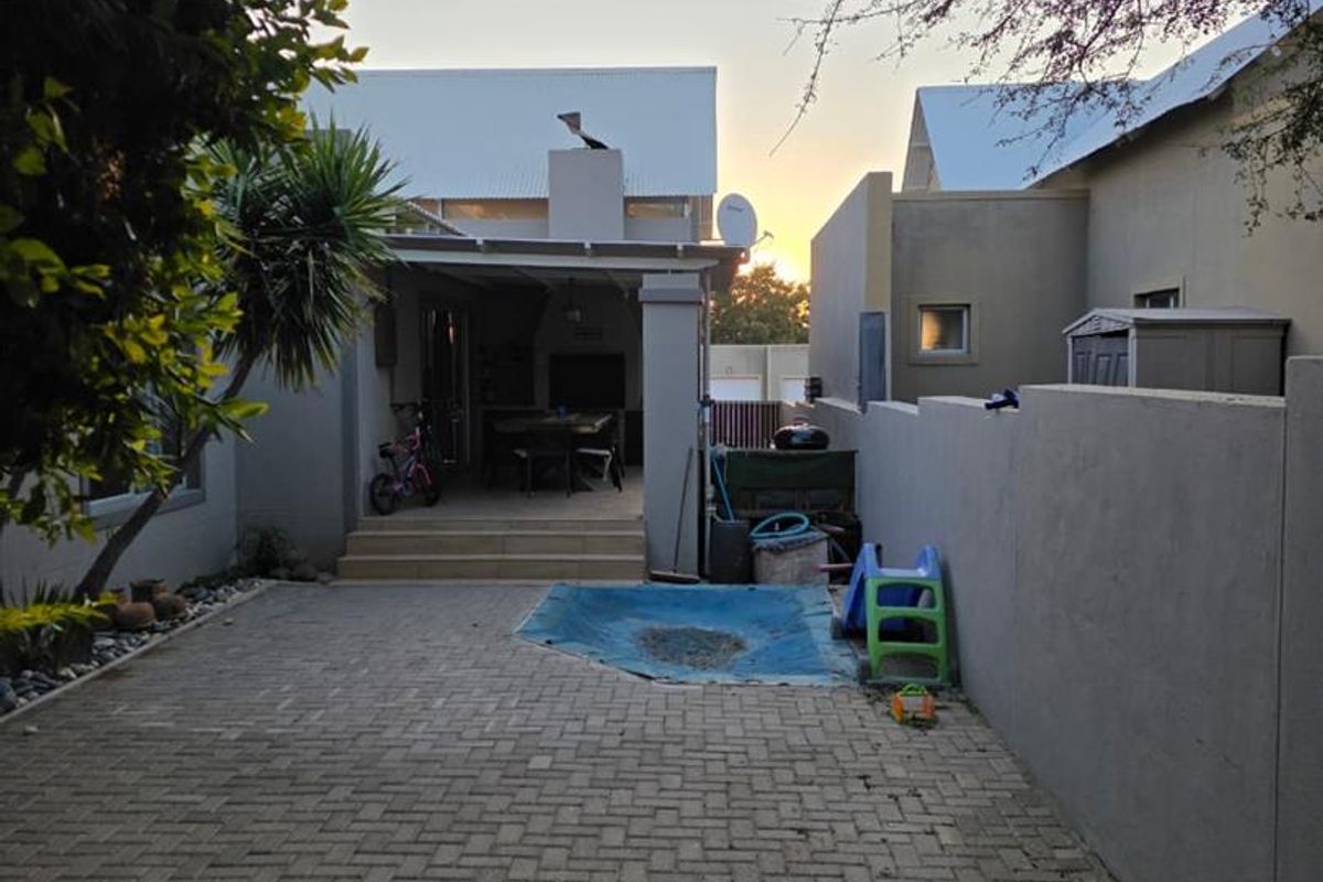 A rear exterior view of the property featuring a paved courtyard area leading to a covered patio space with a built-in braai.