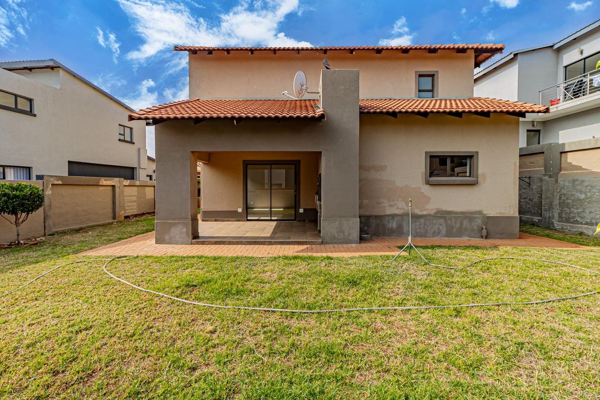 Rear view of the house featuring a covered patio, terracotta tiled roof, and a private garden area with paved patio flooring.