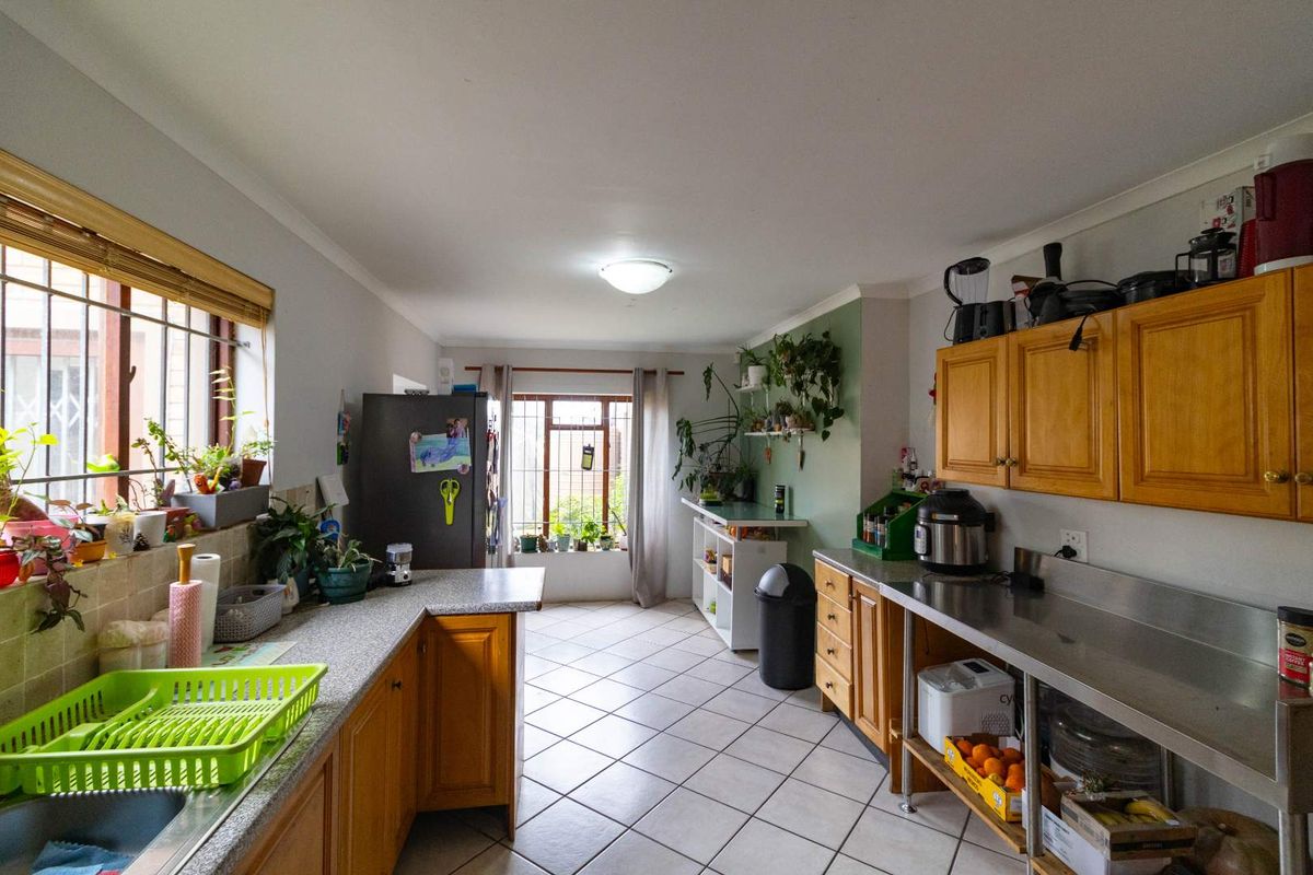 A functional kitchen featuring a mix of laminate and stainless steel countertops, tiled flooring, and wooden cabinetry with security bars on the windows.