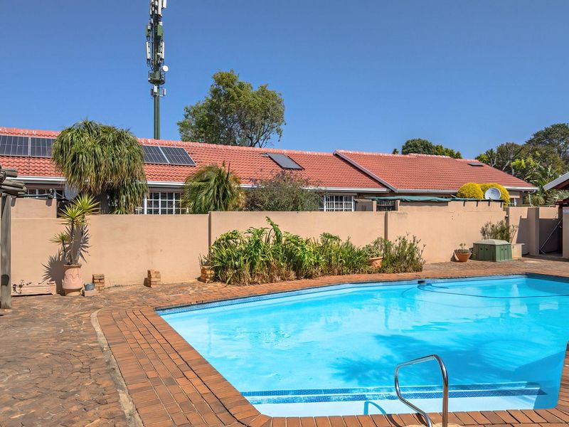 Outdoor pool area featuring a swimming pool, brick paving, and a built-in brick braai, set against a perimeter wall and tiled roof townhouse.