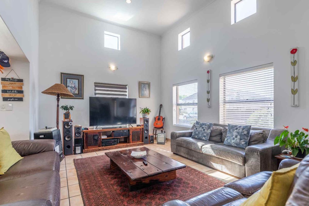 Spacious living room featuring high ceilings, large windows with blinds, and tiled flooring, creating a bright and airy atmosphere.