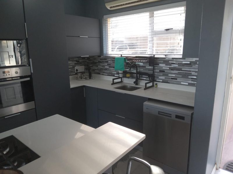 Modern kitchen featuring dark cabinetry, stone countertops, mosaic tile backsplash, built-in oven, microwave, and gas hob with integrated dishwasher space.