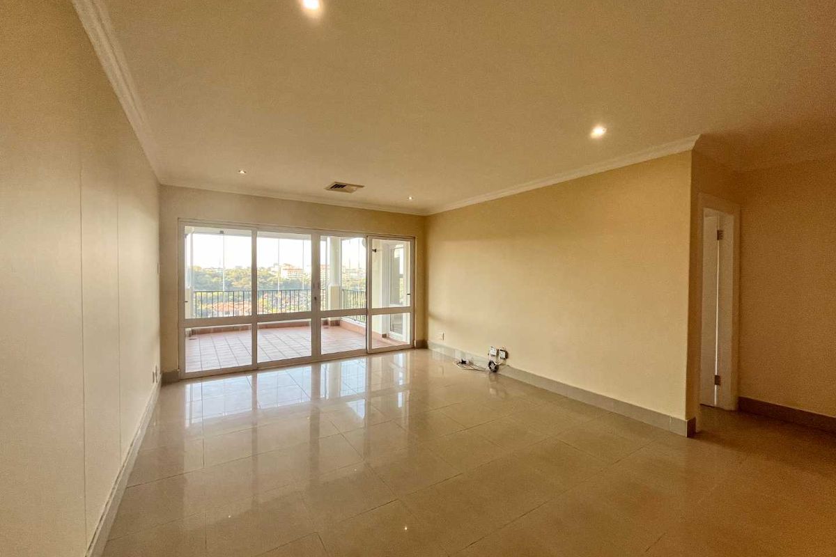 Spacious, empty living area featuring neutral tiled flooring, recessed downlighting, and large sliding glass doors providing access to an attached balcony.