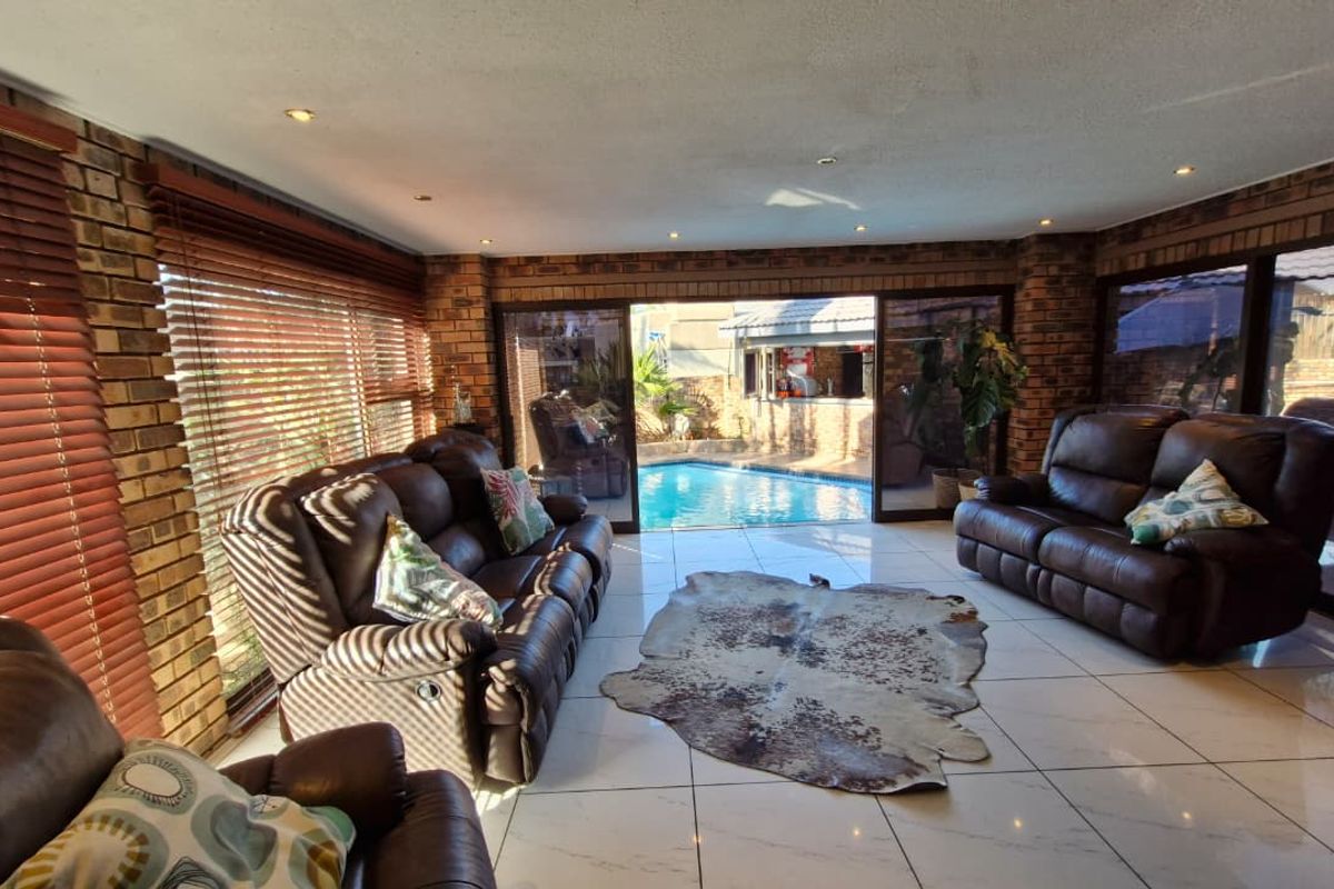 Spacious living room featuring exposed brick walls, tiled flooring, and large sliding glass doors providing direct access to the outdoor pool area.