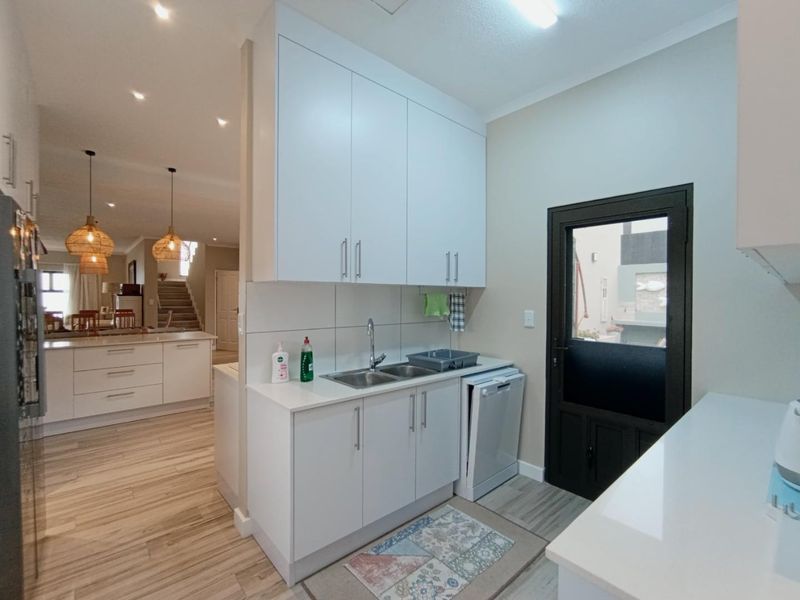 A clean and functional scullery featuring white built-in cabinetry, stone countertops, a double basin sink, and direct access to the exterior.