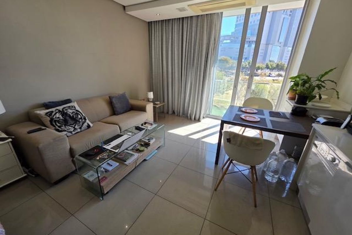 Modern open-plan living and dining area featuring large format floor tiles, recessed ceiling lighting, and floor-to-ceiling sliding doors leading to a balcony.