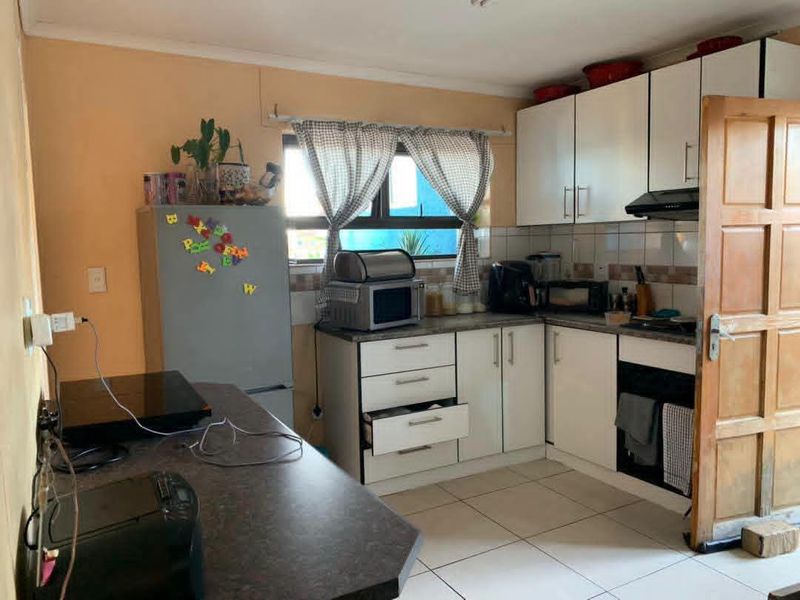 A functional kitchen featuring white cabinetry, laminate countertops, tiled flooring, and a tiled backsplash, offering potential for modernization and cosmetic updates.