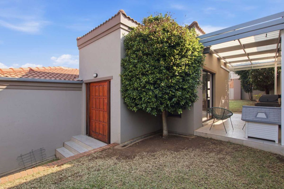 Rear exterior view featuring a paved patio area with a pergola, sliding door access, and a well-maintained boundary wall.