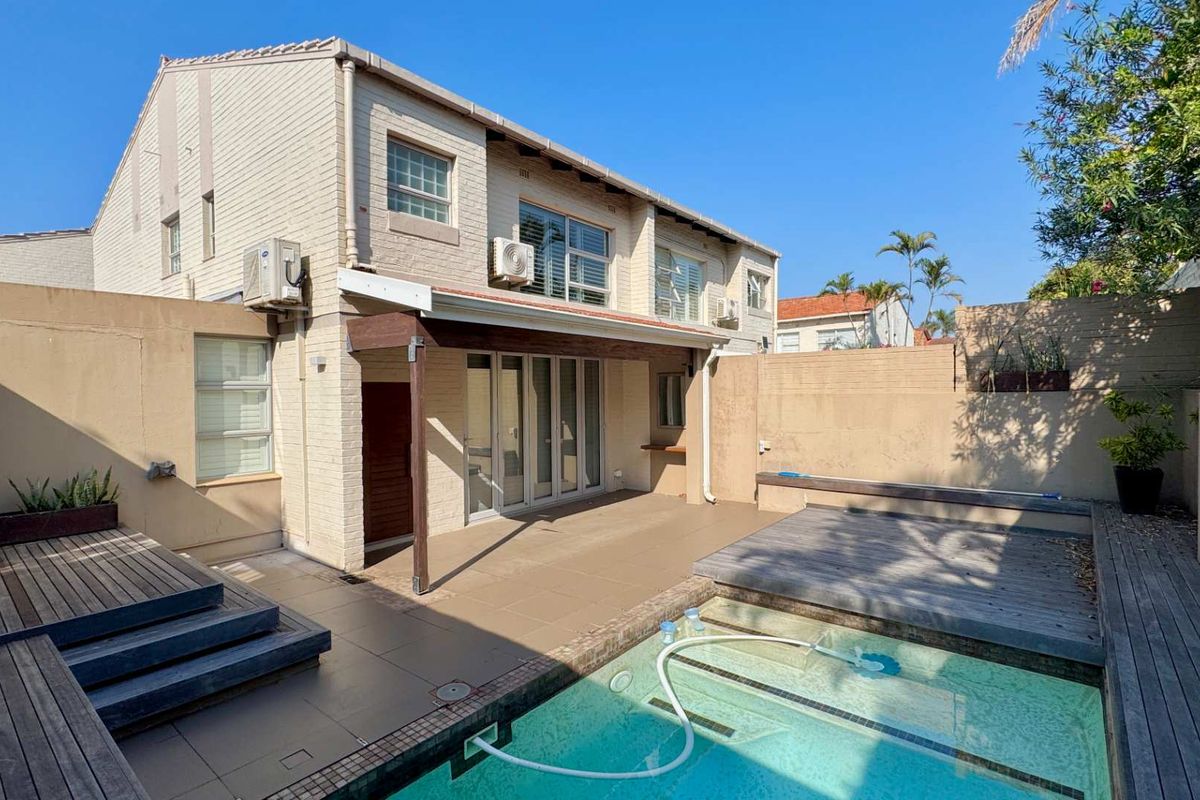 Rear exterior view of the townhouse featuring a private swimming pool, timber decking, and a covered tiled patio area.