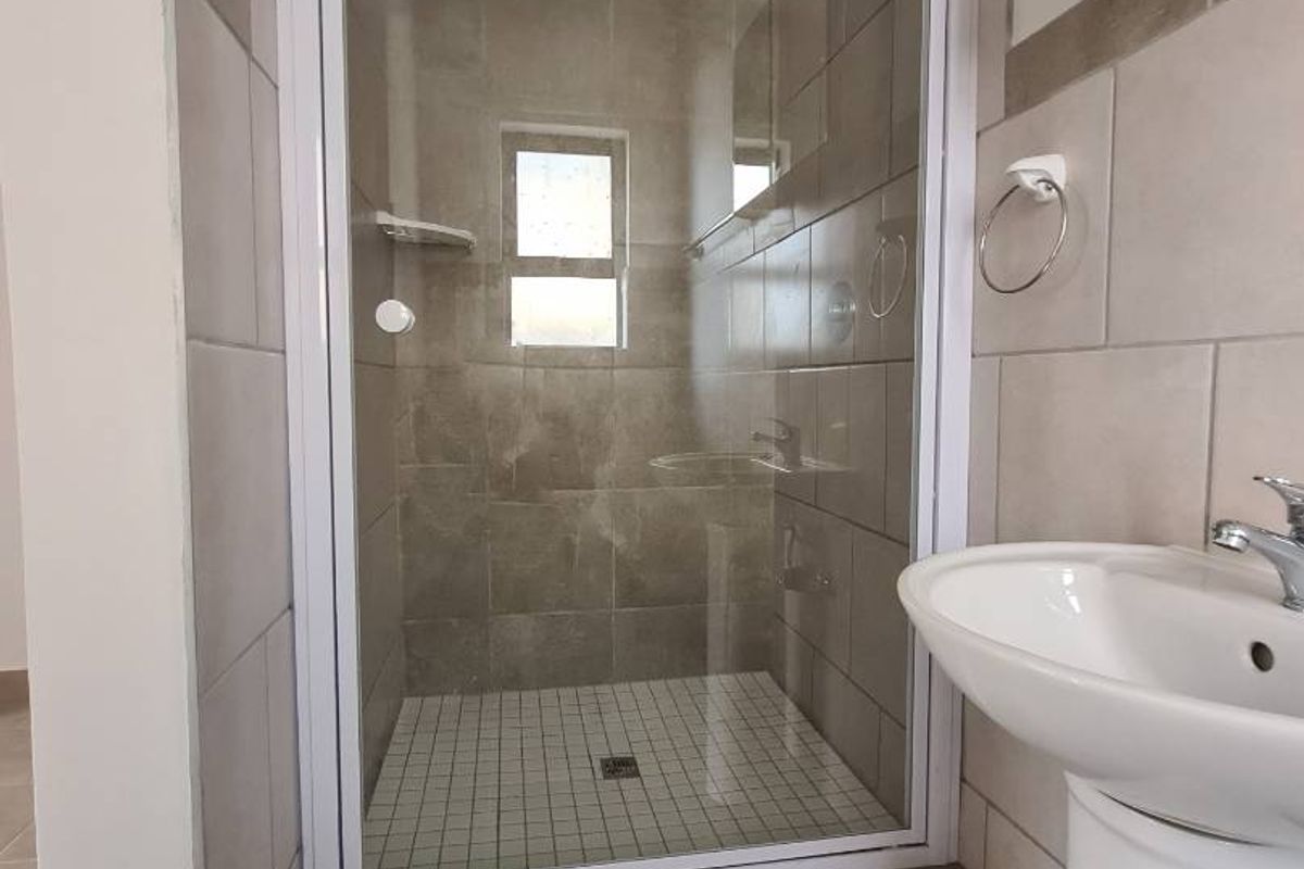A clean, modern bathroom featuring a glass-enclosed shower with tiled walls and a white pedestal basin.