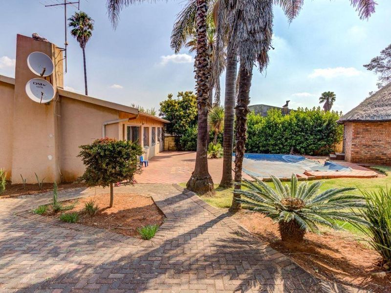Rear exterior view featuring a paved patio area, swimming pool, and a separate thatched roof structure set within a landscaped garden.