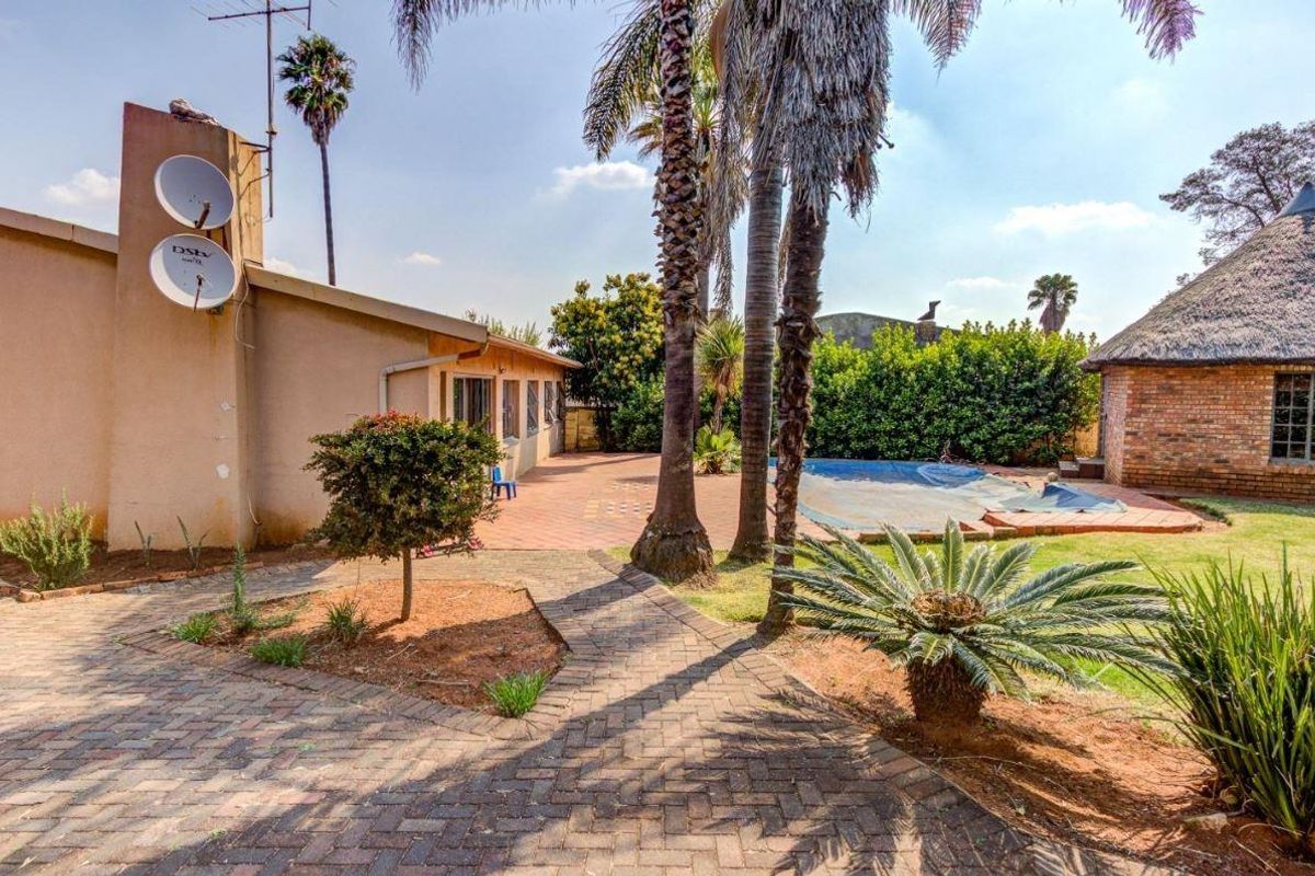 Rear exterior view featuring a paved patio area, swimming pool, and a separate thatched roof structure set within a landscaped garden.