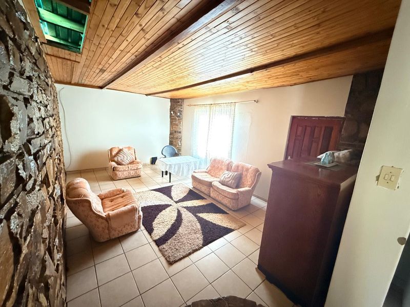 Living room featuring a distinctive stone feature wall, timber-clad ceiling with a skylight, and tiled flooring, offering a rustic aesthetic.