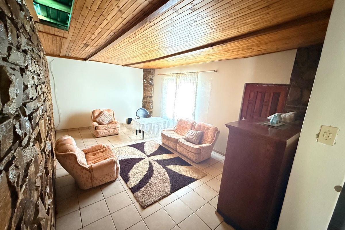 Living room featuring a distinctive stone feature wall, timber-clad ceiling with a skylight, and tiled flooring, offering a rustic aesthetic.