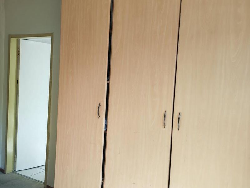 A bedroom featuring a large built-in wooden wardrobe and carpeted flooring, presenting a dated aesthetic in need of cosmetic updates.