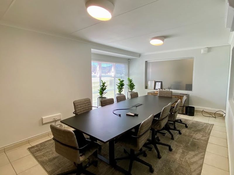 A professional office boardroom featuring tiled flooring, flush mount lighting, and an internal glass partition, providing a clean and functional workspace environment.