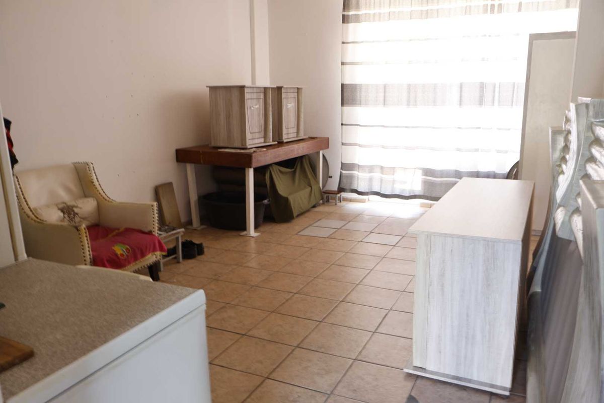 A living area featuring tiled flooring and a large window, currently used for storage with visible wear on the floor tiles.