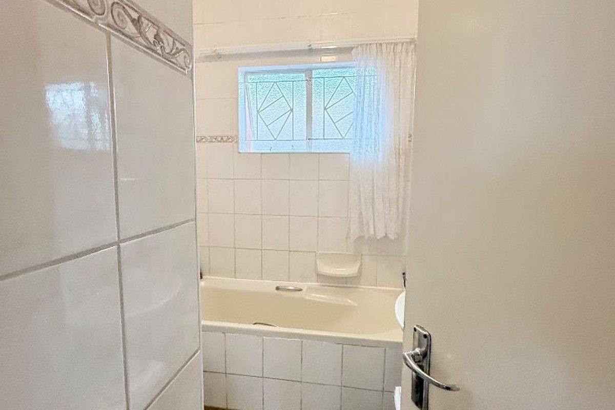 A functional bathroom featuring a built-in bathtub, tiled walls, and a window, viewed from the doorway.