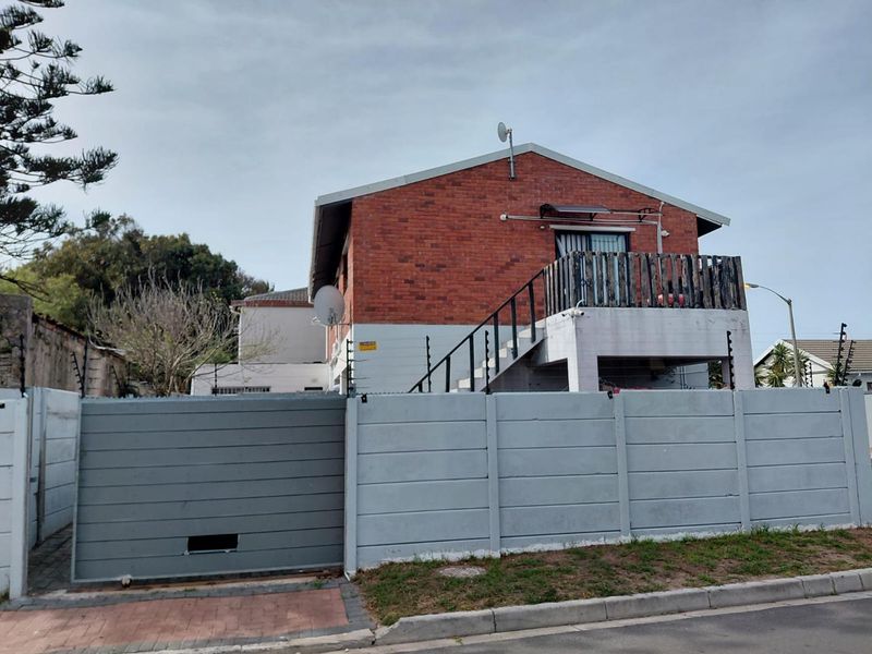Front exterior view of a brick house featuring a secure boundary wall, sliding gate, external staircase, and an elevated balcony.