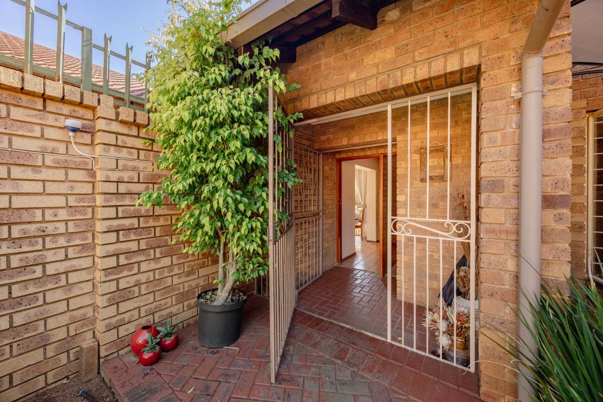 A private rear entrance area featuring facebrick walls, brick paving, and a secure metal gate leading into the home.